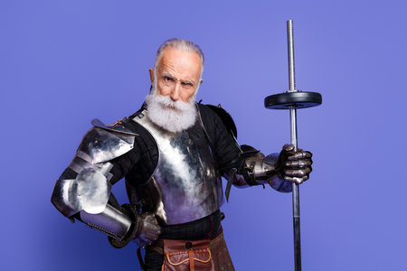 Mature man in medieval knight armor with vibrant beard posing against violet backgroundの写真素材