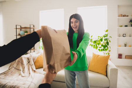 Young woman receives a paper bag delivery with excitement in a cozy and modern interiorの写真素材