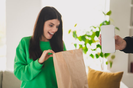 Delighted young woman opening a paper bag in a bright modern homeの写真素材