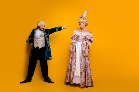 Elegant couple in historic costumes against yellow background, showcasing glamorous and vintage masquerade stylesの写真素材