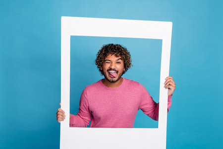 Young man with a happy playful expression, framed in a white border against a blue backgroundの写真素材