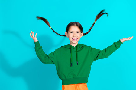 Smiling young girl with braided hair in green hoodie enjoying a colorful turquoise background in a cheerful moodの写真素材