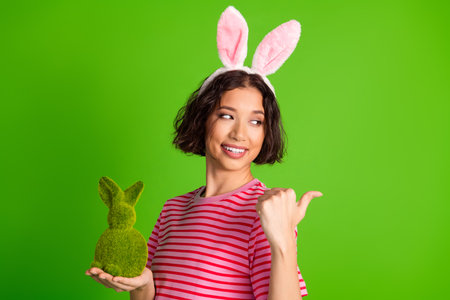 Young woman in striped shirt wearing bunny ears holding decorative rabbit with green backgroundの写真素材