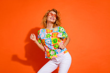 Young woman smiling cheerfully while posing against a vivid orange backdrop wearing a colorful floral print shirtの写真素材