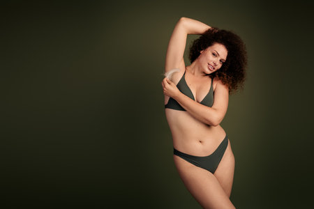 Empowered young woman in green swimwear, showcasing body positivity and natural beauty with confidence on a khaki backgroundの写真素材
