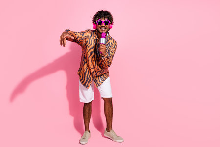 Trendy young man singing karaoke with microphone and colorful glasses on pink background demonstrating fun and stylish lifestyleの写真素材