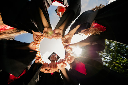 Low angle view portrait of group students touch hands make circle mortarboard gown graduation university outdoorsの写真素材