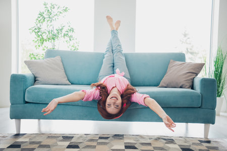 Full length portrait of nice young girl upside down sofa headphones modern white interior flat indoorsの写真素材