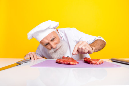 Professional chef inspecting raw meat preparation with focused expression in vibrant kitchen settingの写真素材