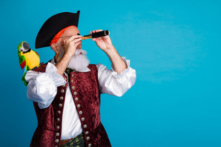 Photo portrait of bearded pirate man hold binoculars tube look empty space wear hallooween costume isolated on blue color backgroundの写真素材