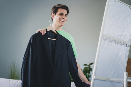 Young man smiling indoors holding a suit jacket, preparing for an important meeting, enjoying a casual momentの写真素材