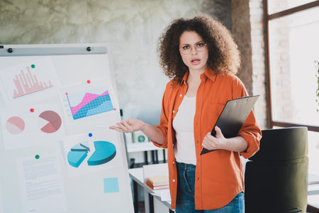 Young professional woman presenting business charts and graphs on a whiteboard in a modern office environment during a team meetingの写真素材