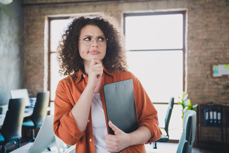 Young businesswoman in casual attire holding a clipboard in a modern office environment,...