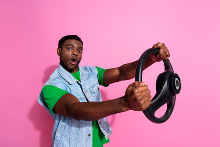 Energetic young man with a steering wheel against a vibrant pink background, expressing excitement and enthusiasm.の写真素材