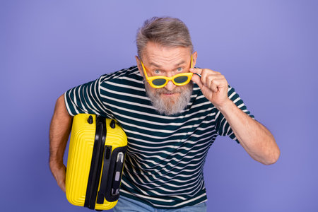 Portrait of a gray-haired man wearing casual style holding suitcase, smiling confidently as he looks into the distanceの写真素材
