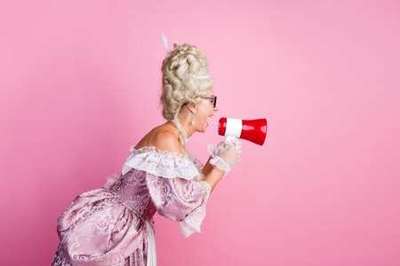 Elegant woman in historical costume shouting through a megaphone against a pink backgroundの写真素材