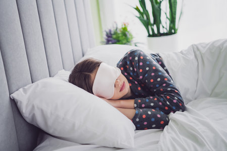 Young Woman Relaxing in Bed with a Sleep Mask, Dressed in Cozy Pajamas, Enjoying Comfort and Tranquilityの写真素材