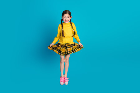 Charming pretty young girl in a yellow sweater posing joyfully against a vibrant blue background,...