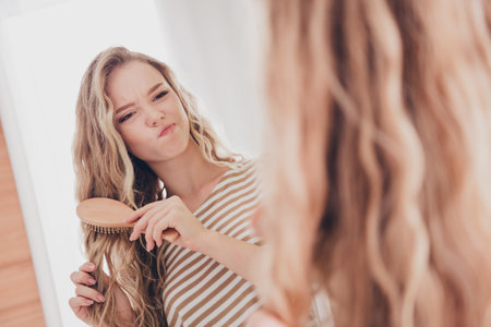 Young woman with blond hair making a playful expression while brushing in the living room during a relaxed weekend at homeの写真素材