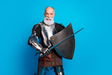 Knight in shining armor with sword and shield posing on vibrant blue background, portraying courage, strength, and historyの写真素材