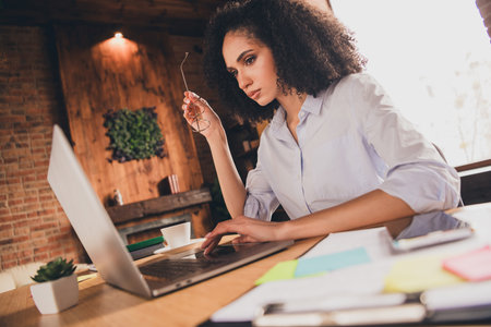 Focused young businesswoman in modern office working on laptop, depicting professionalism and dedication in a stylish setting.の写真素材