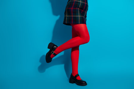 Fashionable young woman in red tights and plaid skirt standing against a bright blue background.の写真素材