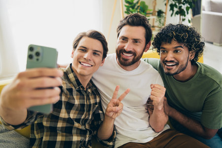 Photo of company three friends smart phone selfie v-sign raise fist hang out weekend modern interior apartment indoorsの写真素材