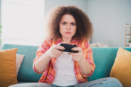 Young woman playing video games while sitting on a couch in a cozy living room, expressing focus and determination during leisure time.の写真素材
