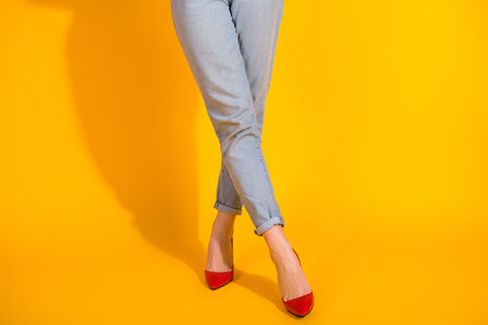 Young woman with stylish jeans standing confidently against bold yellow backgroundの写真素材