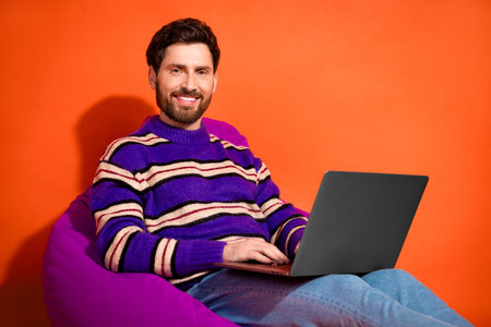 Photo portrait of handsome young guy netbook sit beanbag dressed stylish striped purple garment...