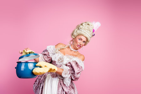 Elegant aristocratic woman in historical costume with funny expression and Victorian hairstyle on pink backgroundの写真素材