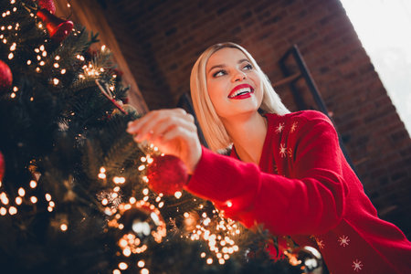 Photo of nice young blonde girl decorate tree wondered wear christmas sweater enjoy cozy x-mas party decoration interior flat indoorsの写真素材