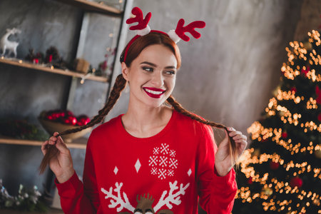 Photo of pretty young girl hold pull braids fantasize wear red christmas festive sweater apartment indoorsの写真素材