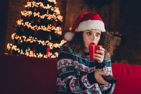 Portrait of nice young woman drink coffee watch tv wear sweater new year xmas garland lights flat indoorsの写真素材