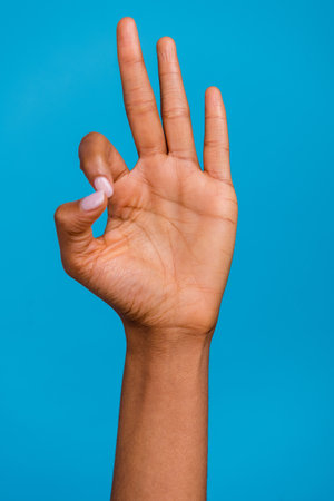 Vertical cropped view of beautiful girl hand showing ok-sign f letter isolated over bright blue color backgroundの写真素材