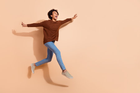 Joyful young african american man jumping against beige background, wearing casual outfit with a big smileの写真素材