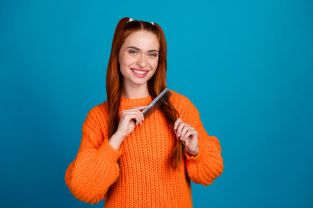 Photo of shiny attractive lady dressed knitted pullover brushing hair empty space isolated blue color backgroundの写真素材