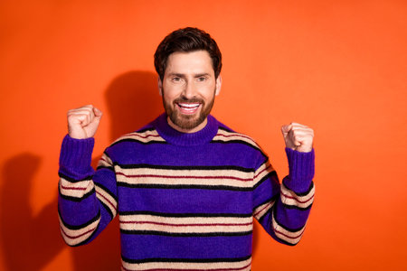 Confident bearded man in striped sweater celebrating success against vibrant background