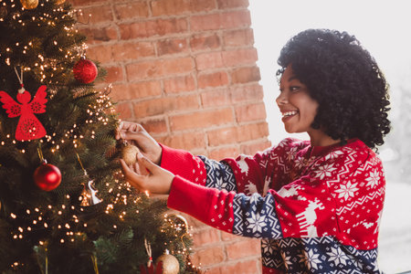 Photo of attractive young woman adorned tree dressed red christmas outfit cozy day light home party decoration interior living roomの写真素材