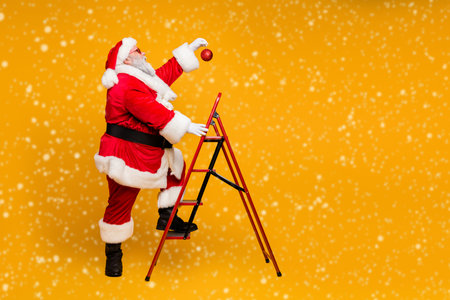 Full body profile side photo of funky funny white beard christmas father climb ladder want hang x-mas decorative tinsels make steps isolated over yellow color backgroundの写真素材