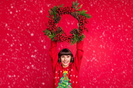 Portrait of attractive cheerful girl holding in hands festal wreath jumping isolated over red color backgroundの写真素材