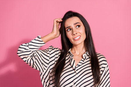 Portrait of a young brunette woman with a confused expression, wearing striped shirt on pink background, depicting casual style and emotionsの写真素材