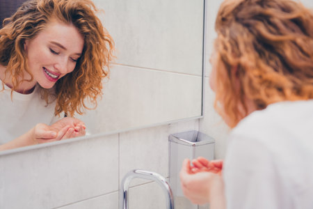 Photo of happy good mood attractive girl in pajamas doing morning routine washing face standing in stylish bathroom indoorsの写真素材