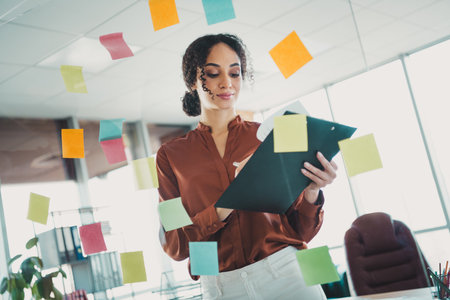 Young professional businesswoman in a modern office setting actively managing tasks surrounded by colorful notesの写真素材