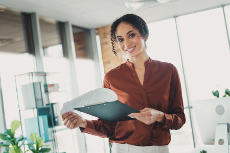 Confident businesswoman reviewing documents in a bright modern office environmentの写真素材