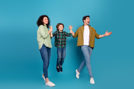 Happy family of three showing excitement together with their young child during a fun day smiling and enjoying a vivid blue backgroundの写真素材