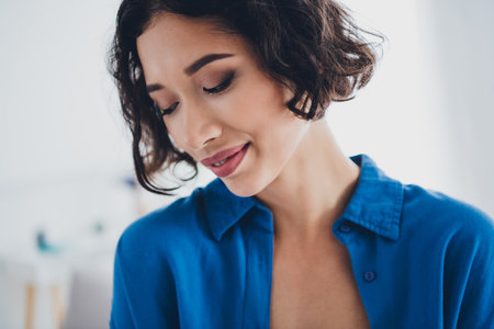 Charming young woman in casual blue shirt enjoys a tranquil moment at home during daylight hours, embracing domestic comfort and leisure.の写真素材