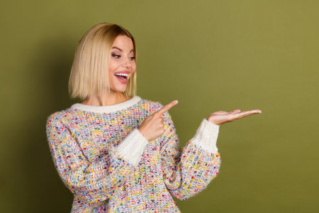 Cheerful young woman gestures, wearing a colorful knit sweater against a khaki background.の写真素材