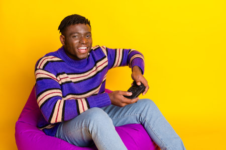 Photo of nice young man sit beanbag play video game wear pullover isolated on yellow color...