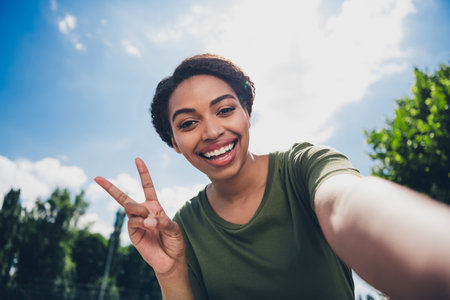 Young woman enjoying outdoors on a sunny day, smiling and showing peace sign during a city walkの写真素材